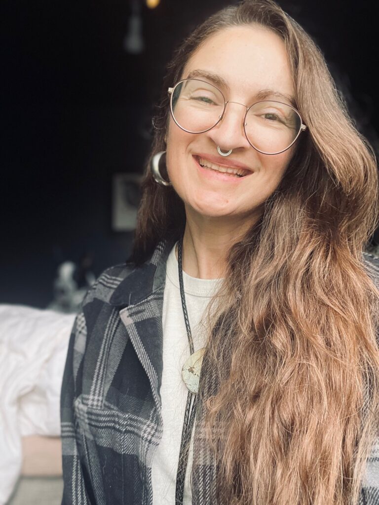 This is a photo of the artist, a smiling, 40-something white women with long brown hair and glasses. 